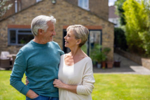 Loving senior couple smiling in front of their house. Reverse mortgage retirement planning for Canadian homeowners 55 and older